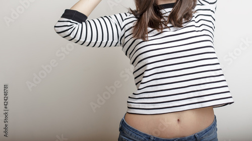 Tableau sur toile Confident girl in blue jeans and a striped sweater, raised her arms and extended her beautiful belly and slender waist