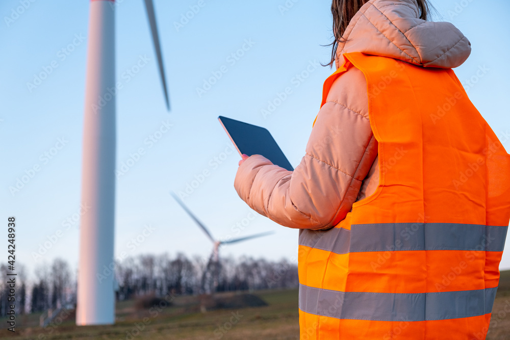 Engineer does maintenance and repairs wind wills or wind turbine using a tablet in the orange vesta. Engineer does maintenance and repairs wind wills or wind turbine using a tablet in the orange vesta.