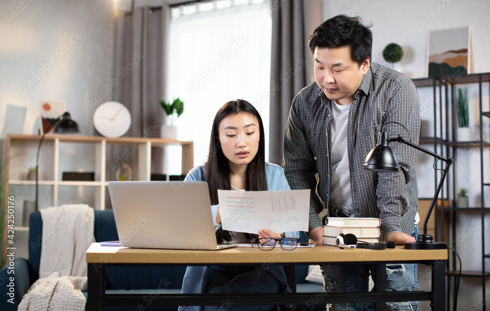 Two asian business partners having working meeting at bright office. Young man and woman discussing financial report and using modern laptop. Two asian business partners having working meeting at bright office. Young man and woman discussing financial report and using modern laptop.
