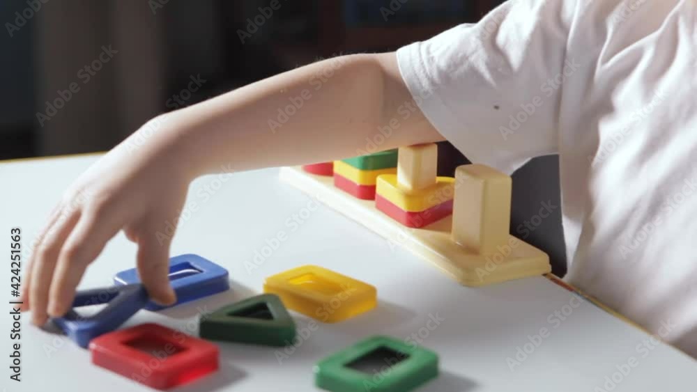 A boy sit At White Table And Play With Sorter at home. A child in a white T-shirt plays educational games. Development of logic, study of shapes and colors. High quality FullHD footage A boy sit At White Table And Play With Sorter at home. A child in a white T-shirt plays educational games. Development of logic, study of shapes and colors. High quality FullHD footage