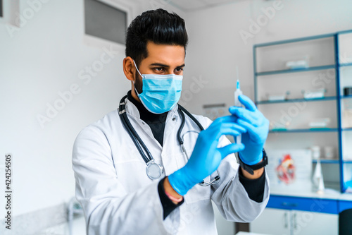Portrait of an Indian male doctor with an injection in his hands and in a protective mask  he is preparing to vaccinate patients. Modern medicine  Asian doctor