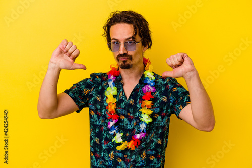 Young caucasian man wearing a hawaiian necklace isolated on yellow background feels proud and self confident, example to follow.