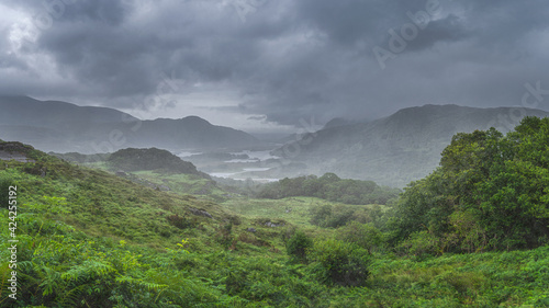 Atmospheric, dramatic storm sky and clouds, mist and heavy rain in Irish iconic viewpoint, Ladies View. Green valley with lake. Rink of Kerry, Ireland