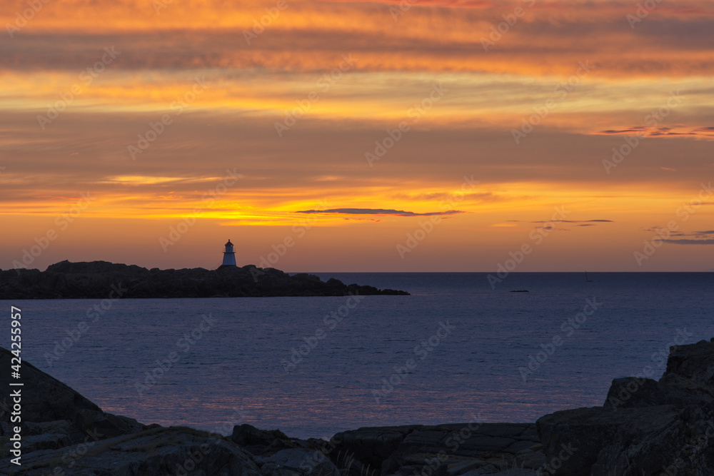 Colorful sunset on the coast of Northern Sea. A lighthouse in the far distance and stunning clouds litted by the sunseting sun in red, orange and pink. Last rays of light. Landscape, background.