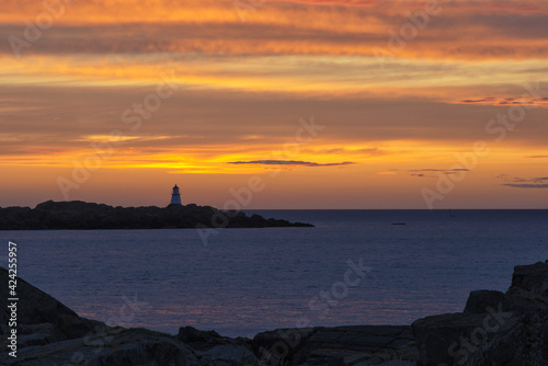 Colorful sunset on the coast of Northern Sea. A lighthouse in the far distance and stunning clouds litted by the sunseting sun in red, orange and pink. Last rays of light. Landscape, background.