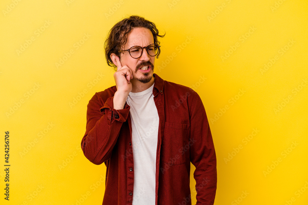 Young caucasian man isolated on yellow background covering ears with hands.
