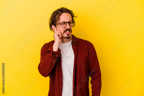 Young caucasian man isolated on yellow background covering ears with hands.