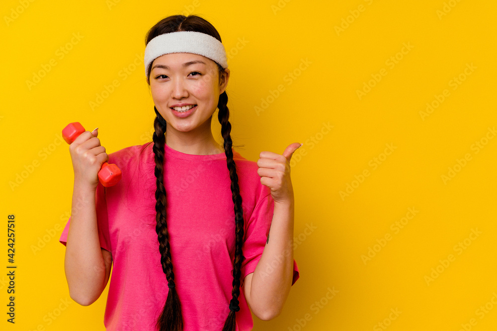 Young sport chinese woman isolated on yellow background smiling and raising thumb up Young sport chinese woman isolated on yellow background smiling and raising thumb up