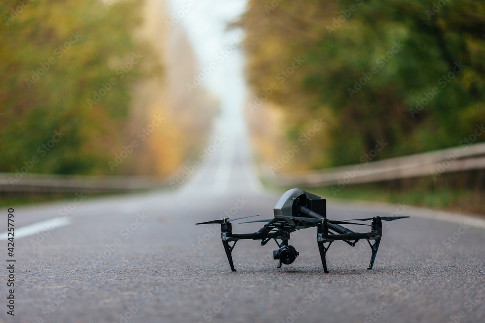 Fototapeta premium At the autumn dawn, a drone flies over the asphalt road going into the distance
