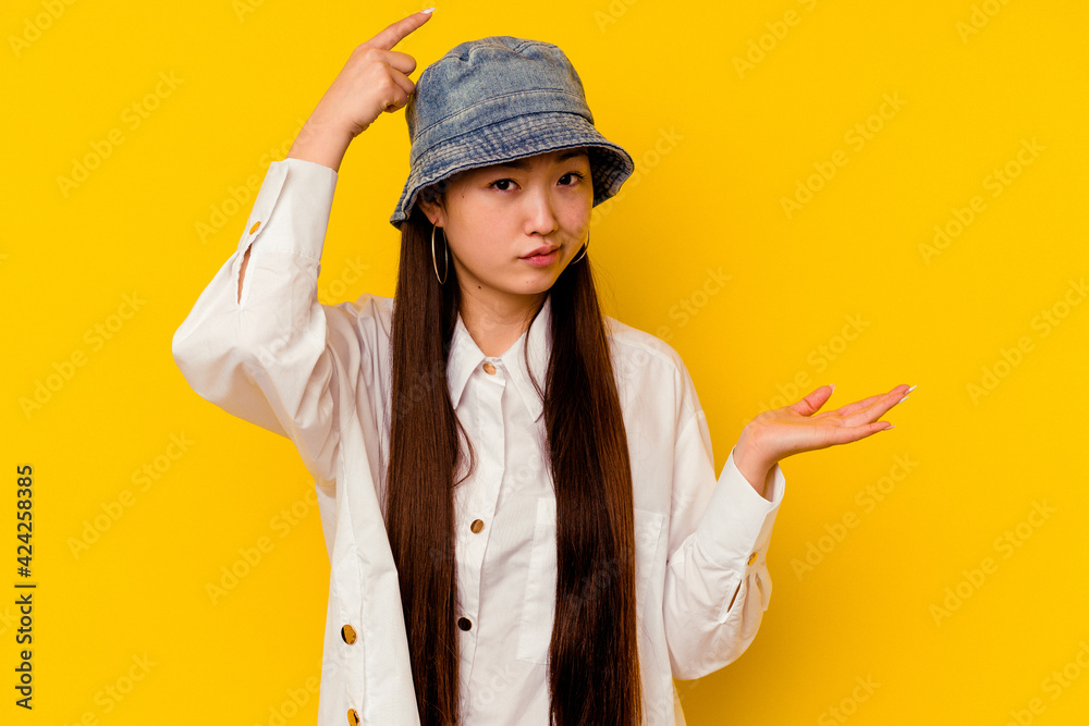 Young chinese woman isolated on yellow background holding and showing a product on hand. Young chinese woman isolated on yellow background holding and showing a product on hand.