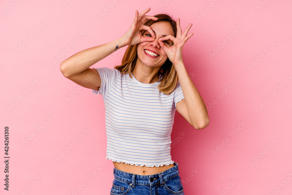 Young caucasian woman isolated on pink background showing okay sign over eyes