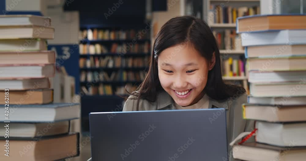 Asian schoolgirl studying on laptop and smiling sitting in school library Asian schoolgirl studying on laptop and smiling sitting in school library