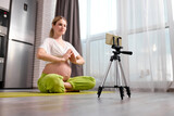 young caucasian pregnant woman sit doing exercises on floor and recording video