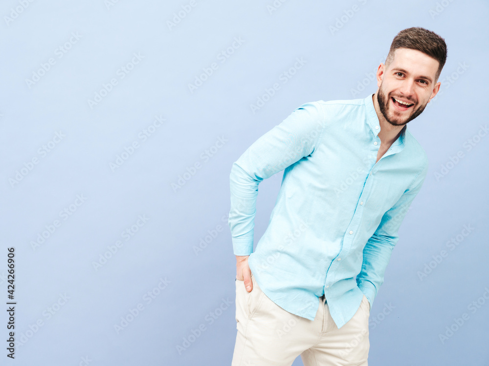 Portrait of handsome smiling hipster lumbersexual businessman model wearing casual shirt and trousers. Fashion stylish man posing against purple wall in studio