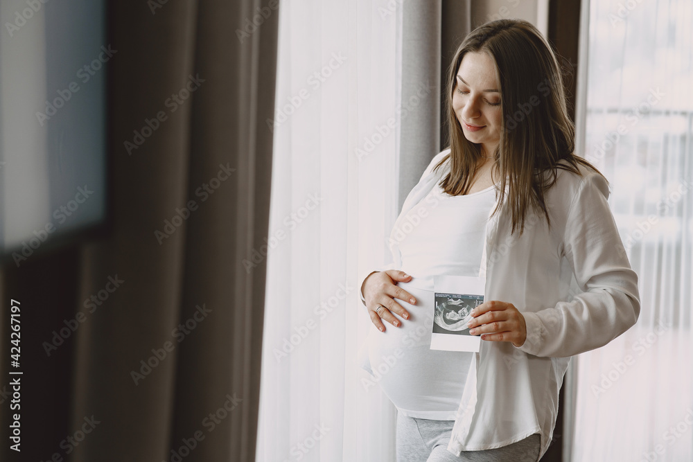 Pregnant woman stands by the window and looks at photo Pregnant woman stands by the window and looks at photo