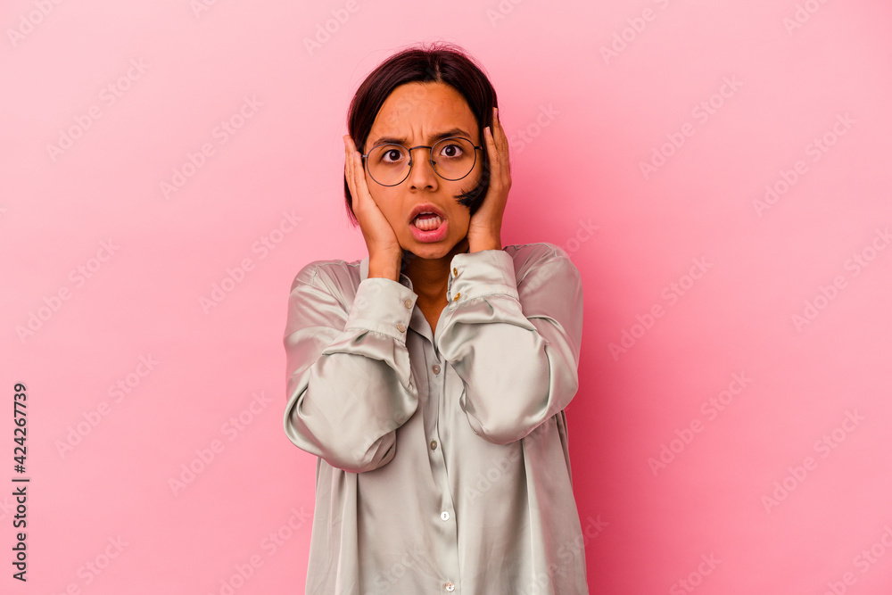 Young mixed race woman isolated on pink background covering ears with hands trying not to hear too loud sound.