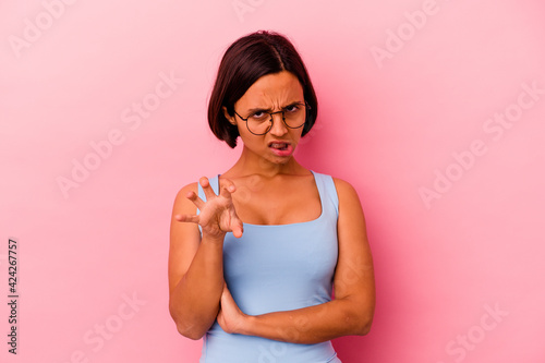 Young mixed race woman isolated on pink background showing claws imitating a cat, aggressive gesture. © Asier
