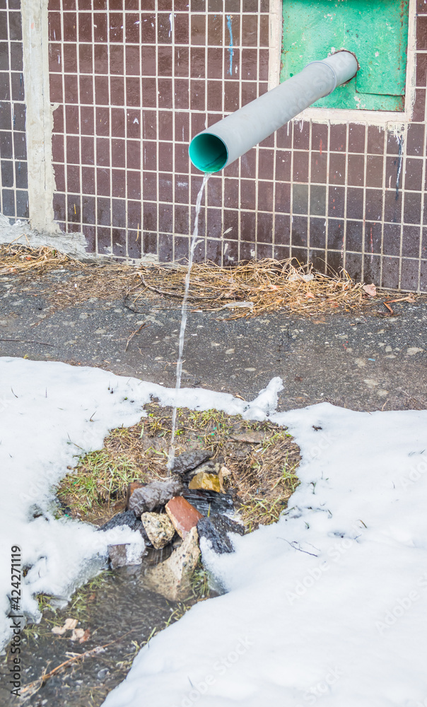 Naklejka premium Water flows from the roof of the building through a drainpipe. Early spring and melting snow.