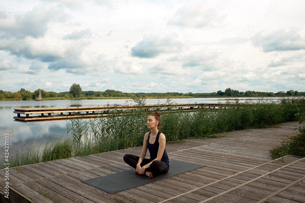 Attractive young woman or model meditating and practicing yoga on the pier near lake. Attractive young woman or model meditating and practicing yoga on the pier near lake.