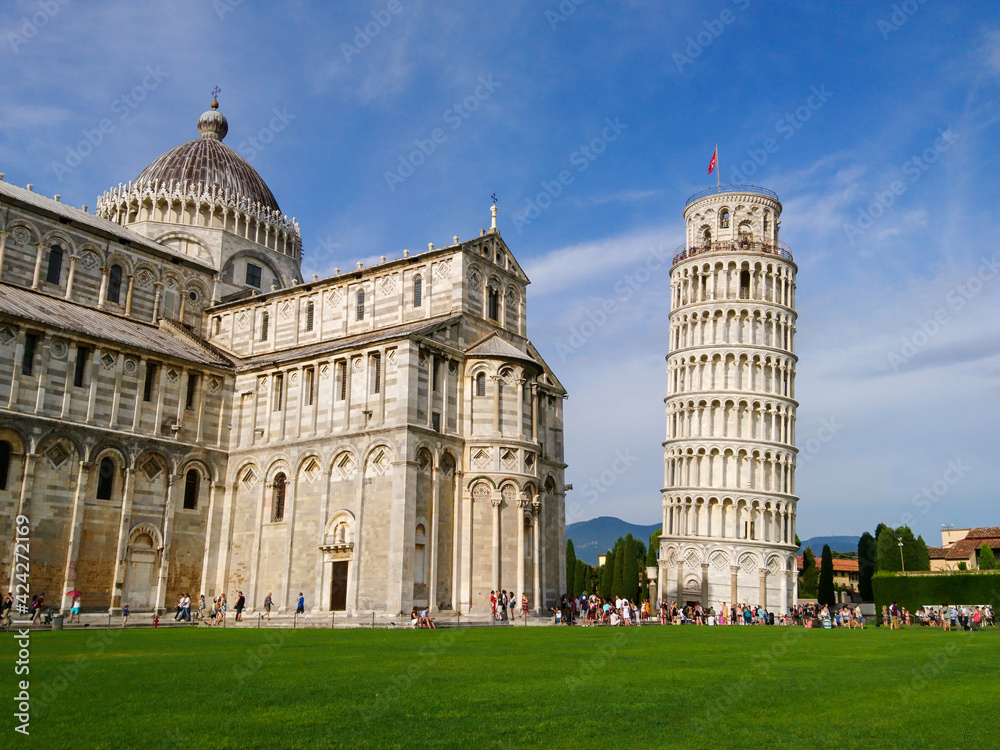 Leaning Tower of Pisa (elaborately adorned 14th-century tower) and Cathedral di Pisa (marble-striped cathedral) on summer green grass and blue sky. Travel Italy, famous places