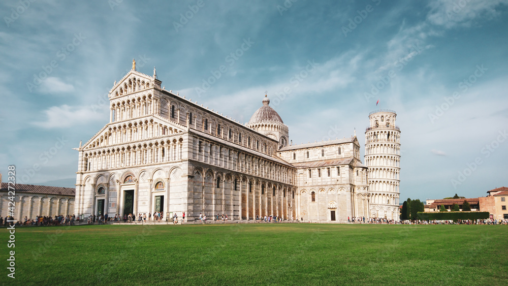 Leaning Tower of Pisa (elaborately adorned 14th-century tower) and Cathedral di Pisa (marble-striped cathedral) on summer green grass and blue sky. Travel Italy, famous places. Color graded