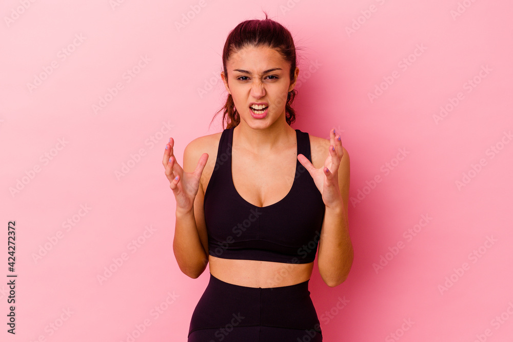 Young sport Indian woman isolated on pink background upset screaming with tense hands.