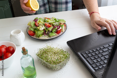 A woman prepares a green vegan salad according to a lesson from the Internet. Online cooking concept. Horizontal orientation.