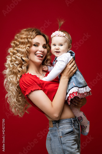 Playful stylish lady posing with her child on red background