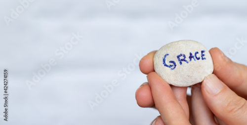 Woman's hand holding stone with handwritten word grace against white background with copy space for text. Biblical concept of God Jesus Christ mercy and love.