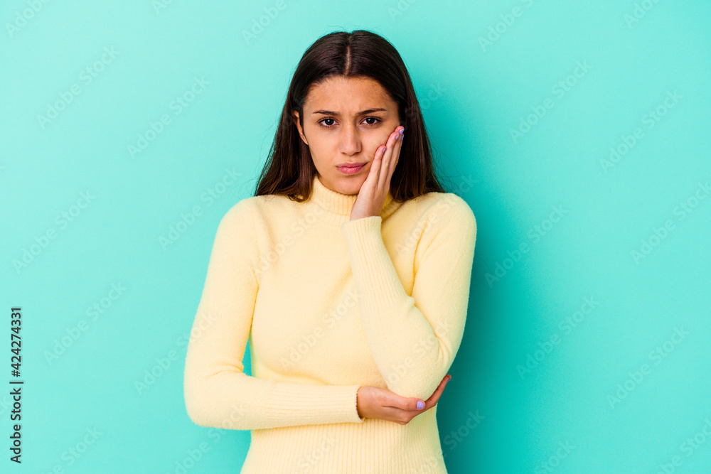 Obraz premium Young Indian woman isolated on blue background blows cheeks, has tired expression. Facial expression concept.