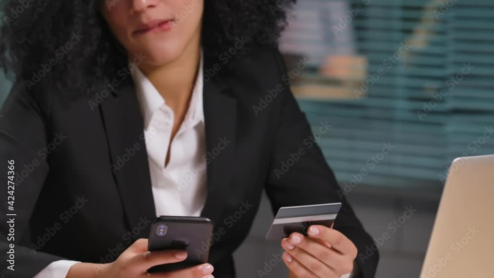 Portrait of African American woman makes an online purchase using credit card and smartphone. Businesswoman posing at workplace in office. Close up. Slow motion ready 59.94fps. Portrait of African American woman makes an online purchase using credit card and smartphone. Businesswoman posing at workplace in office. Close up. Slow motion ready 59.94fps.
