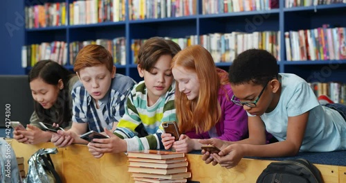 Multiethnic students using mobile phone in library at school