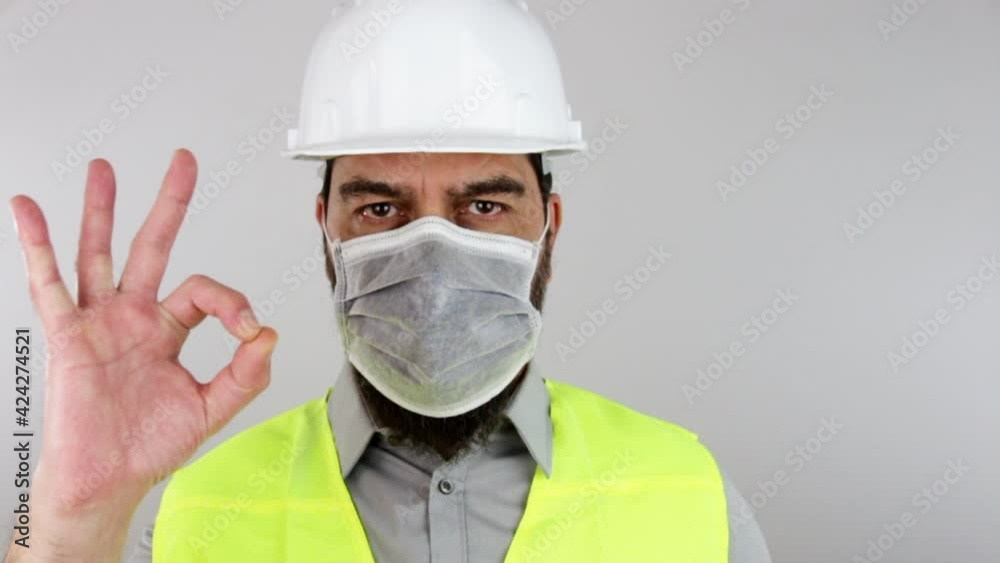 Civil engineer wearing work helmet and protective mask doing ok sign with hand on isolated white background. Slow motion.