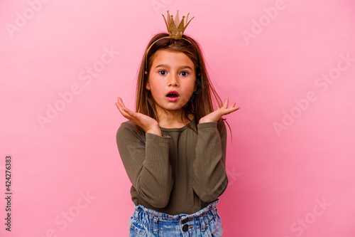 Little princess girl with crown isolated on pink background surprised and shocked.