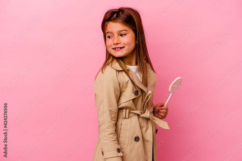 Little caucasian girl holding a lollipop isolated on pink background looks aside smiling, cheerful and pleasant. Little caucasian girl holding a lollipop isolated on pink background looks aside smiling, cheerful and pleasant.