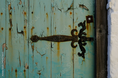Peeling and rusty door and hinge with a white wall to the left.