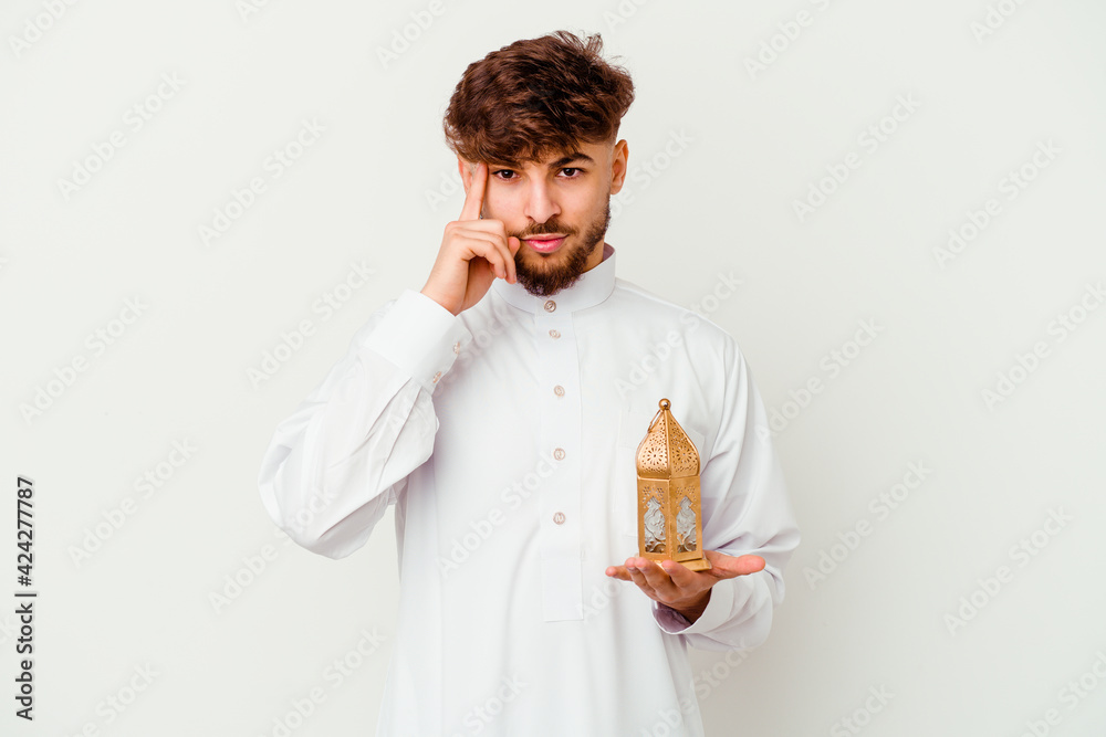 Young Moroccan man wearing a typical arab clothes holding a ramadan lamp isolated on white background pointing temple with finger, thinking, focused on a task. Young Moroccan man wearing a typical arab clothes holding a ramadan lamp isolated on white background pointing temple with finger, thinking, focused on a task.