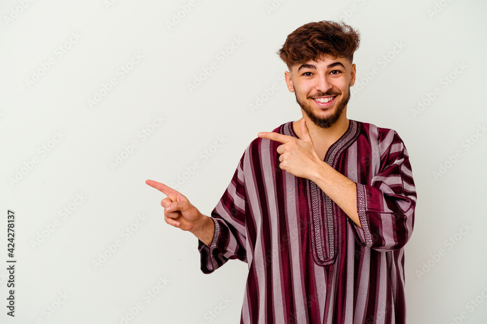 Young Moroccan man isolated on white background pointing with forefingers to a copy space, expressing excitement and desire.