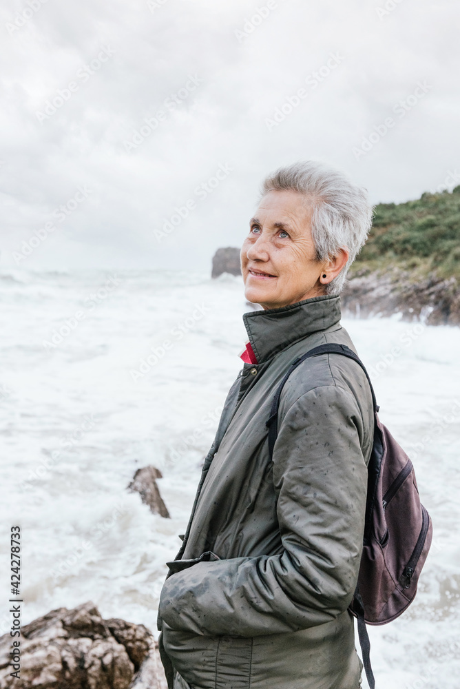 portrait of senior woman enjoying her retirement taking a walk along the beach on a cloudy day with strong waves. pensioner looking at camera. active senior people. portrait of senior woman enjoying her retirement taking a walk along the beach on a cloudy day with strong waves. pensioner looking at camera. active senior people.