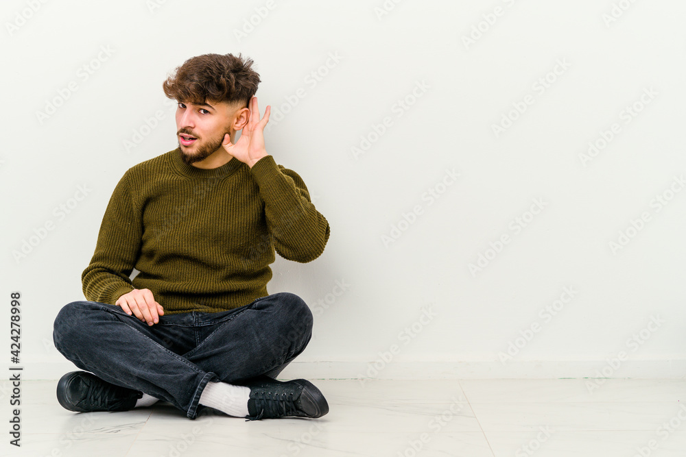 Young Moroccan man sitting on the floor isolated on white background trying to listening a gossip. Young Moroccan man sitting on the floor isolated on white background trying to listening a gossip.