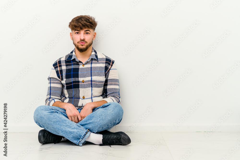 Young Moroccan man sitting on the floor isolated on white background sad, serious face, feeling miserable and displeased.