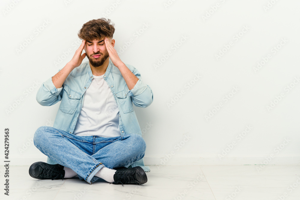 Young Moroccan man sitting on the floor isolated on white background touching temples and having headache. Young Moroccan man sitting on the floor isolated on white background touching temples and having headache.