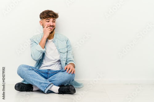 Young Moroccan man sitting on the floor isolated on white background relaxed thinking about something looking at a copy space. © Asier