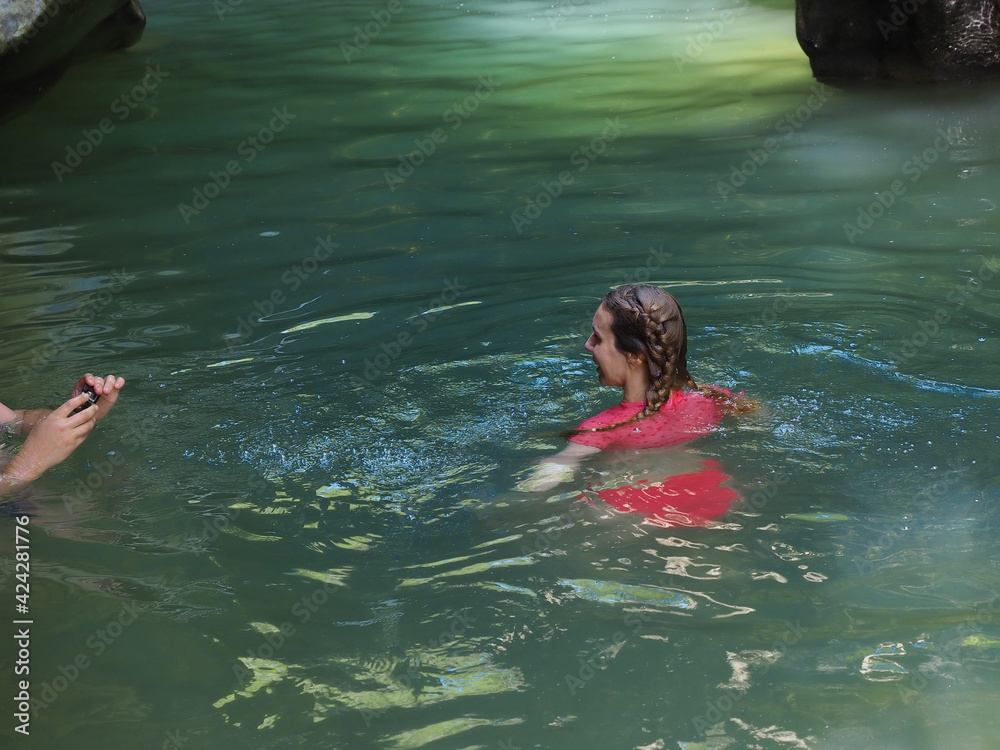 A girl poses for the camera swimming in a turquoise river of a rocky gorge