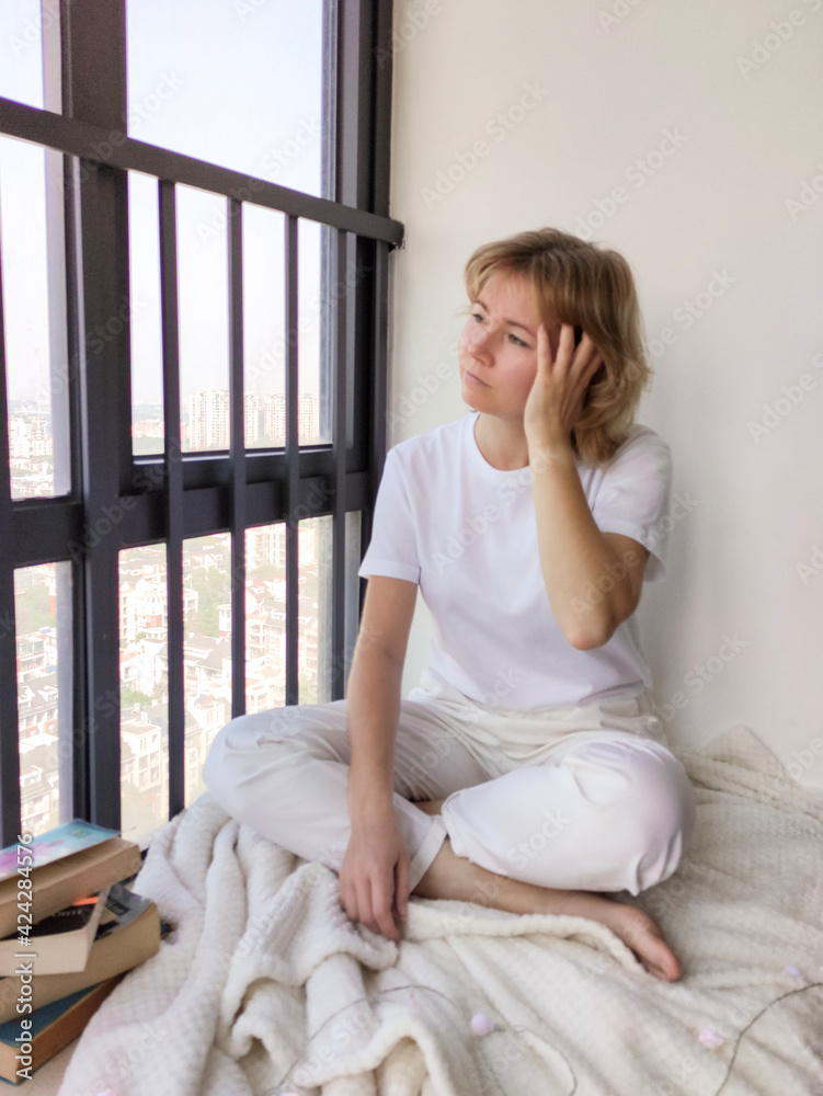 Attractive young woman sitting on the windowsill and looking through window Attractive young woman sitting on the windowsill and looking through window
