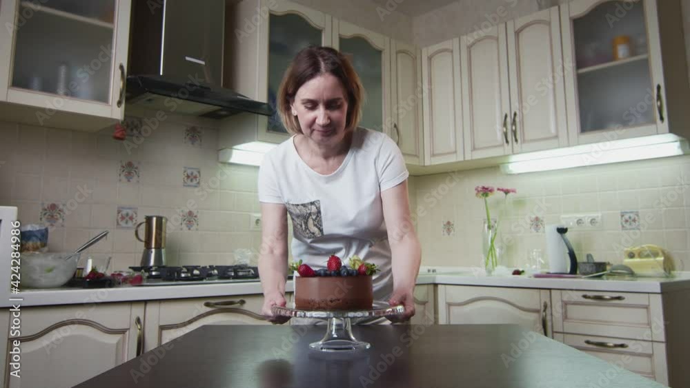 Housewife woman puts hit a new chocolate cake on the table at kitchen Housewife woman puts hit a new chocolate cake on the table at kitchen