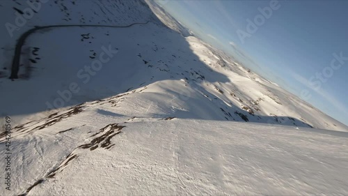 Epic FPV drone dive down a snowcovered mountain towards road and sunset in national park, Langvatnet, Oppljostunnelen photo