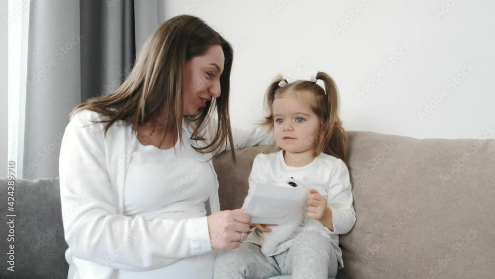Pregnant mother sitting on couch with her little daughter Pregnant mother sitting on couch with her little daughter