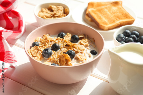 Healthy breakfast of whole wheat flakes with milk, blueberries and toast close-up on wooden table. Selective focus