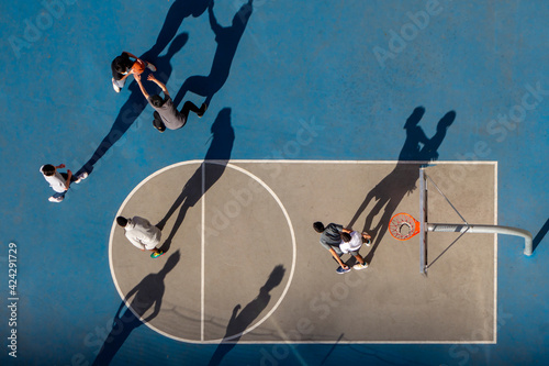 young man playing basketball at dusk or morning light with long shadows high angle bird's eye view